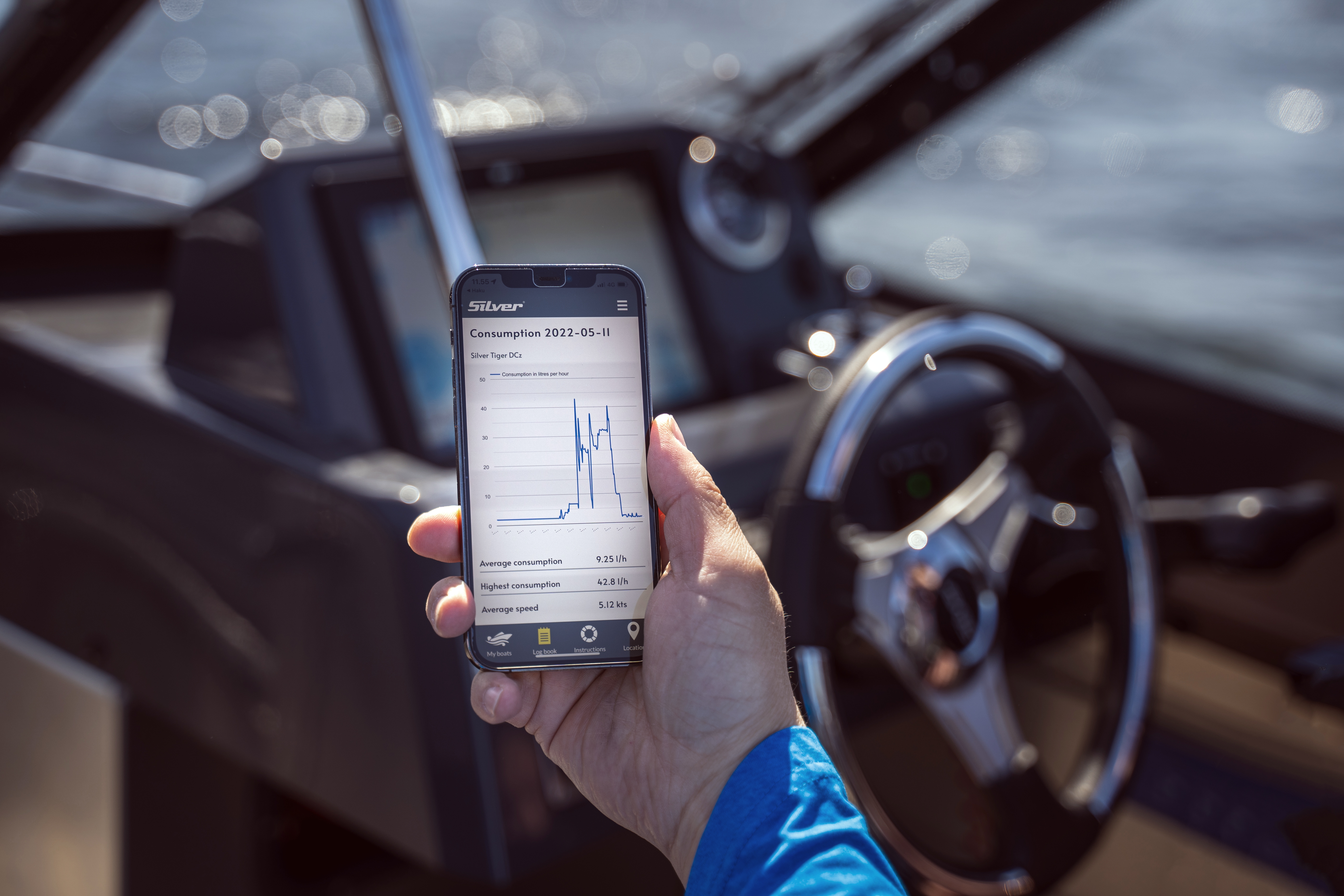 Käsi pitää älypuhelinta, jossa näkyy avattuna MySilver-mobiilisovellus. Silver-veneen ohjaamo näkyy sumeana taustalla.